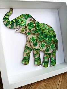 an elephant made out of green and white paper in a shadow box on a wooden floor