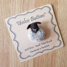 a small black and white sheep brooch sitting on top of a wooden table next to a card