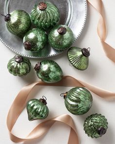 some green glass ornaments are on a plate and pink ribbon is in the bowl next to them