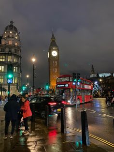 two people are standing on the sidewalk in front of a busy city street at night