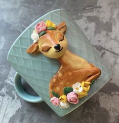 a deer figurine sitting on top of a blue cup with flowers around it