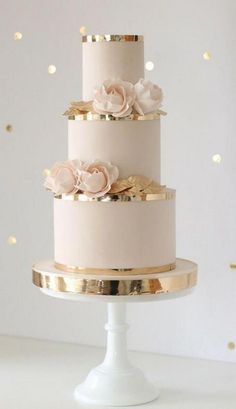 a three tiered cake with gold trim and pink flowers on the top is sitting on a white pedestal