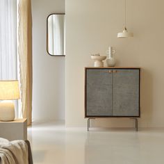 a white room with a cabinet, mirror and lamp on the sideboard in it