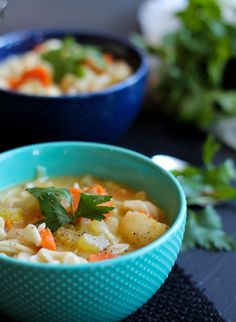 two bowls of soup with carrots, potatoes and parsley on the top one bowl is blue