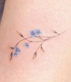 small blue flowers on the side of a woman's thigh, with leaves and stems