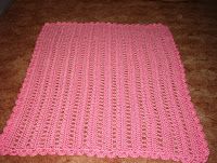 a pink crocheted blanket laying on the floor