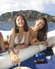 two women sitting on the back of a boat with drinks and snacks in front of them