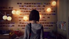 a woman standing in front of a wall with pictures on it and lights hanging from the ceiling