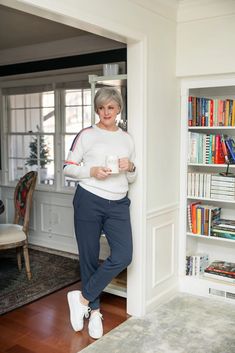 an older woman leaning against a bookcase holding a coffee cup in her right hand