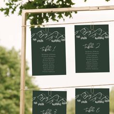 wedding seating chart hanging from a wooden frame with trees in the back ground and greenery behind it