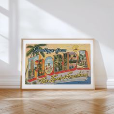 an old florida travel poster hangs in the corner of a room with wood floors and white walls