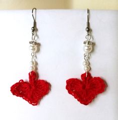 red crocheted heart earrings with pearls hanging from hooks on white surface next to wall