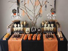 a table topped with lots of halloween treats and desserts next to a tree filled with bats