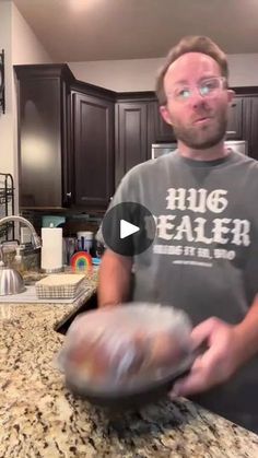 a man holding an object in his hand while standing next to a kitchen counter top