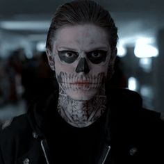 a man with a skull on his face in a hallway, looking at the camera