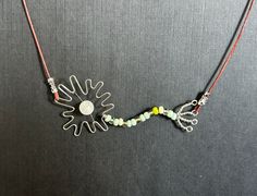 a necklace made with wire and beads on a gray surface, featuring an image of the sun