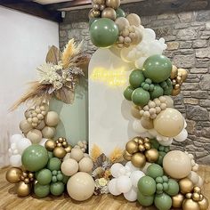 an arch made out of balloons and greenery on a wooden floor in front of a stone wall