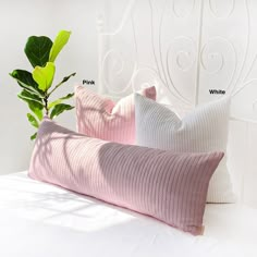 two pink and white pillows sitting on top of a bed next to a green plant