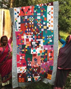 two women holding up a colorful quilt in the woods