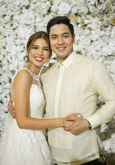 a man and woman standing next to each other in front of a flower covered wall