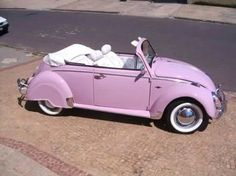 an old pink car parked on the side of the road