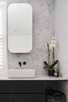 a white sink sitting under a bathroom mirror next to a black cabinet and vase with flowers