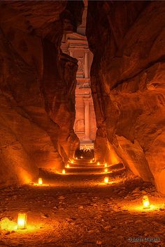 candles are lit in the middle of a narrow passage between two large rock formations, with columns on either side