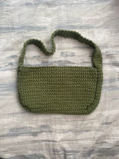 a green crocheted purse sitting on top of a white bed cover covered in sheets