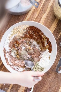 a person mixing ingredients in a bowl on a wooden table with utensils and measuring spoons