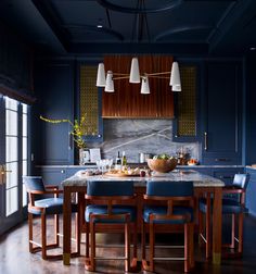 a kitchen with dark blue walls and wooden furniture, along with an island table surrounded by blue upholstered chairs