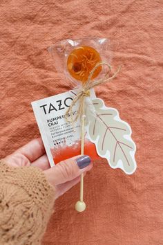 a person is holding an orange lollipop on a stick with a tag attached to it