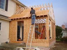 a man standing on top of a ladder in front of a house that is under construction