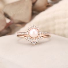 a pink pearl and diamond ring sitting on top of a pillow