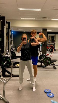 two people in a gym doing exercises with their hands up to the side, and one person taking a selfie