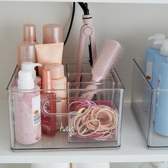 two clear bins filled with different types of hair products and personal care items on top of a white counter