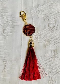 This is a gold-colored alloy pendant, featuring a piece of gold and dark red brocade fabric sealed in epoxy resin, with a matching gold heart lobster clasp and dark red tassel. Comes with gift bag. Great gift! I can make more to order. Red Tasseled Jewelry As A Gift, Red Tasseled Jewelry For Gift, Gold Rectangular Bag Charm For Gift, Rectangular Gold Bag Charm For Gift, Elegant Gold Bag Charm As Gift, Elegant Gold Bag Charm For Gift, Gold Bag Charm With Lobster Clasp As Gift, Elegant Bag Charm With Lobster Clasp As Gift, Elegant Bag Charm With Lobster Clasp For Gift