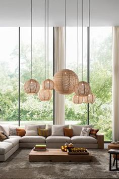 a living room filled with lots of furniture and large windows covered in hanging light shades