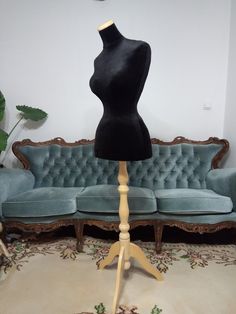 a black mannequin on a wooden stand in front of a blue velvet couch