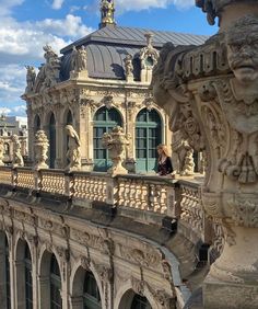 a woman standing on top of a balcony next to a building with statues and windows