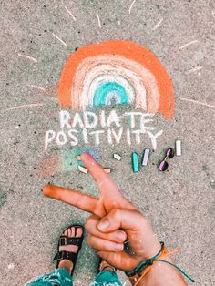 someone pointing at the word radiate positivity written in chalk on concrete