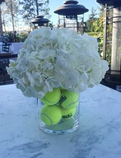 a glass vase filled with tennis balls on top of a marble table covered in white hydrangeas