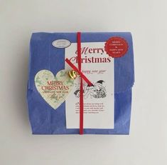 a blue wrapped gift box with a red ribbon tied around it and a heart shaped ornament