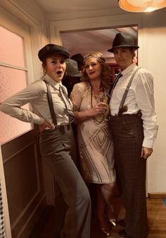 three women standing next to each other in front of a door wearing hats and suspenders