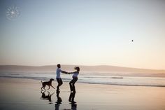 two people and a dog on the beach with their hands in each others's pockets