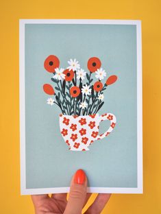 a hand holding up a card with flowers in a teacup on the front and bottom