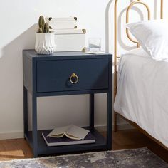 a blue nightstand with an open book on it next to a white bed in a bedroom