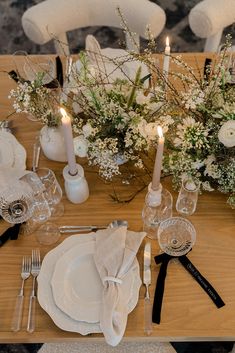 the table is set with white flowers and black napkins, silverware and candles