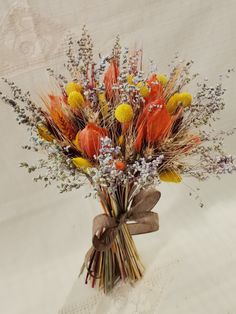 a bouquet of dried flowers in a vase on a white tablecloth covered cloth background