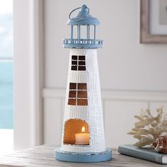 a small white lighthouse with a lit candle in it on a table next to some seashells