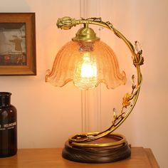 a table lamp sitting on top of a wooden table next to a bottle and painting